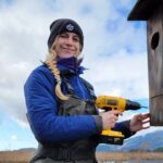 Amanda Wik holding a drill at a nesting box in a salt marsh