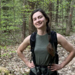 Olivia Kurz, wearing a backpack, standing in an open area of a forest