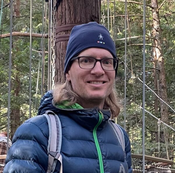 Man standing in front of trees wearing a hat